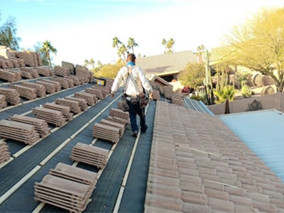 Roofer walking on a roof prepared with underlayment and staged stacks of concrete tiles